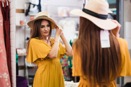 Cô gái mặc váy vàng đứng trước gương thử chiếc mũ